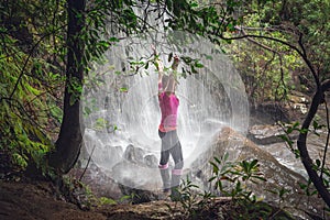 Female standing in waterfalls with lush ferns, trees in bushland