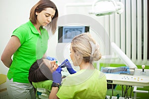 Female stomatologist in protective gloves examining patient`s teeth. Dentist caries treatment at dental clinic office