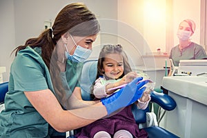 Female stomatologist showing little girl how correctly brushing teeth