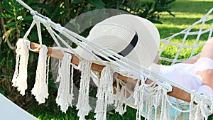 female in a straw hat is resting in a hammock around the palm trees and enjoying the tranquility and relaxation