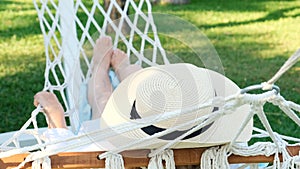 female in a straw hat is resting in a hammock around the palm trees and enjoying the tranquility and relaxation