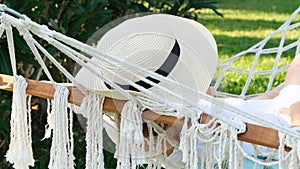 female in a straw hat is resting in a hammock around the palm trees and enjoying the tranquility and relaxation