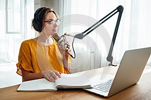 Female streaming his audio podcast using microphone and laptop at his small broadcast studio