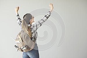 Female student arms raised with backpack on grey background