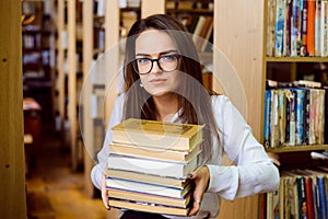 Female student with a big pile of books in the library