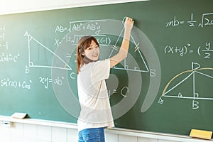 Female student in the classroom writing on chalkboard  mathematical equations