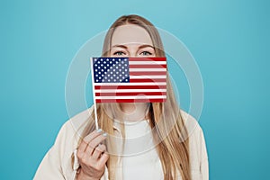 female student covering her face with a small american flag. Caucasian blonde woman holds a small american flag isolated