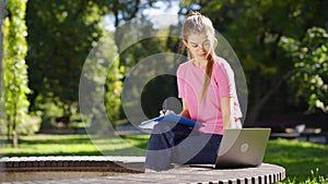 Female student doing homework in park using laptop