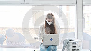 Female student with face mask sitting in a laundromat using laptop