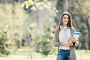 Female student girl outside with headphones walking with notebooks in park