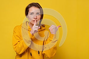 Female student holding finger on lips mouth to keep it quiet secret hush pointing at copy space