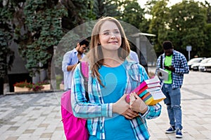 The female student is holding a stack of books outdoors
