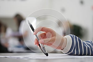 Female student holds a pen in her hand while sitting at a desk in a classroom. Writing a dictation, solving a problem, testing or