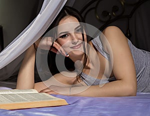 Female student laying in bed and read book, girl dreaming about life