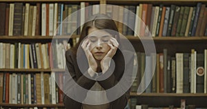 Female student, library. Sad girl stands before the book shelves in the library