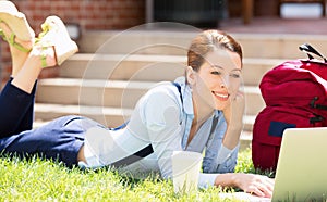 Female student lying down on lawn grass working on laptop