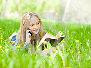 Female student lying on grass reading a book and talking on the green grass