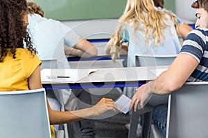 Female student passing note to friend in classroom