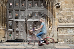 Female Student Riding Old Fashioned Bicycle Around Oxford University College Buildings With Motion Blur