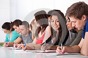 Female student sitting with classmates writing at desk photo