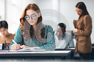 Female student sitting at desk in classroom writing exam