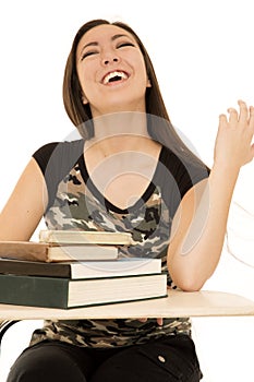 Female student sitting at desk full of books laughing