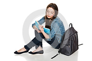 Female student sitting on floor with backpack reading a book