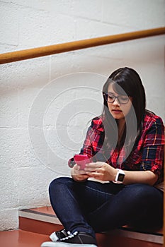 Female student sitting on staircase and using mobile phone