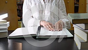 Female student studying in a library, sitting and reading a braille book