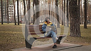 Female student studying remotely in park, using laptop computer. Woman working on laptop outdoor. Female freelancer sitting on ben