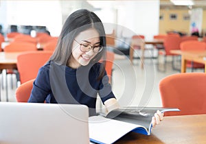 Female student taking notes from a book at library