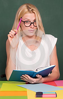 Female student taking notes from a book at library. Female teacher sitting at her workplace and teaching English