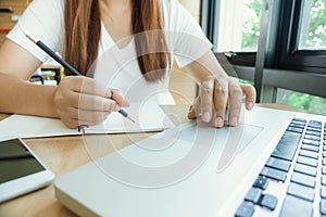 Female student taking notes from a book at library. Young asian woman sitting at table doing assignments in college library.