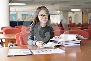 Female student taking notes from a book at library, Young asian woman sitting at table doing assignments in college library