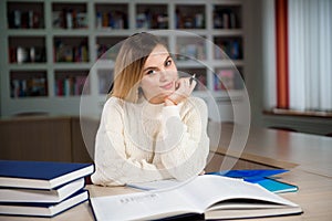 Female student taking notes from a book at library. Young woman sitting at table doing assignments in college library.