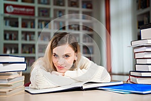 Female student taking notes from a book at library. Young woman sitting at table doing assignments in college library.