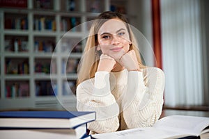 Female student taking notes from a book at library. Young woman sitting at table doing assignments in college library.