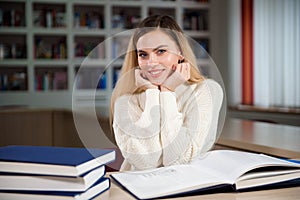 Female student taking notes from a book at library. Young woman sitting at table doing assignments in college library.