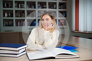 Female student taking notes from a book at library. Young woman sitting at table doing assignments in college library.