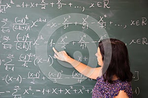 Female student or teacher in the classroom writing on chalkboard mathematical equations