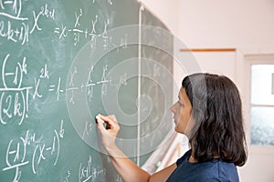 Female student or teacher in the classroom writing on chalkboard mathematical equations