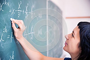 Female student or teacher in the classroom writing on chalkboard mathematical equations