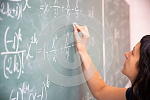 Female student or teacher in the classroom writing on chalkboard mathematical equations