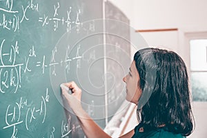 Female student or teacher in the classroom writing on chalkboard mathematical equations