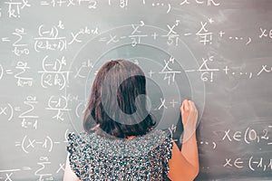 Female student or teacher in the classroom writing on chalkboard mathematical equations