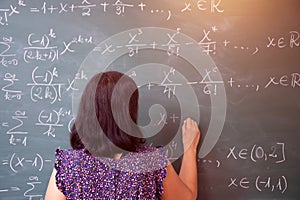 Female student or teacher in the classroom writing on chalkboard mathematical equations