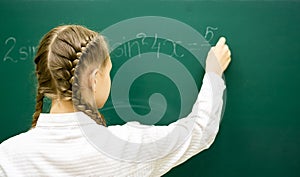 Female student teenager at a math lesson writing in chalk on a blackboard. Education, adolescence, high schoo