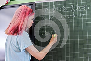 Female student teenager at a math lesson writing in chalk on a blackboard