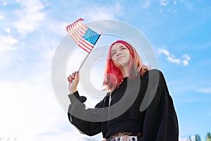 Female student teenager with USA flag in hand, blue sky with clouds background.