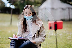 female student virtual learning on mobile wearing face mask internet outdoors